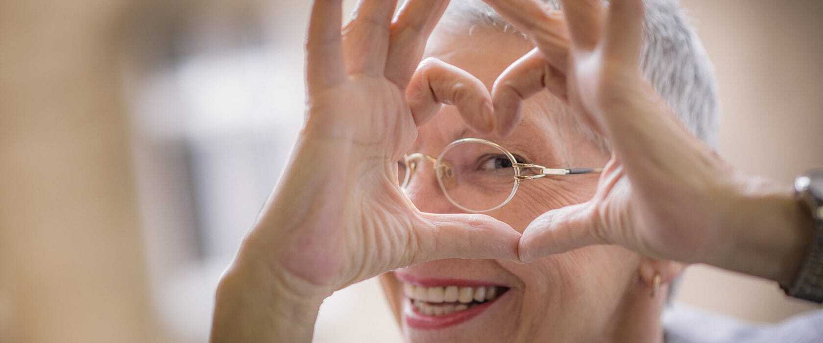 J2711_1680x700_BlogImage1_Love-and-Communication Senior woman making a heart shape with her fingers