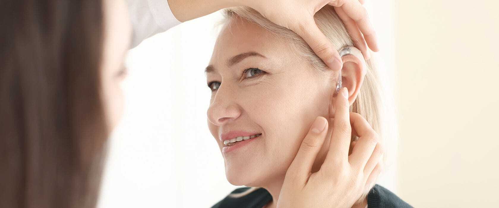 J2496_HA_1680x700_Update Doctor inserting a hearing aid into a senior woman's ear