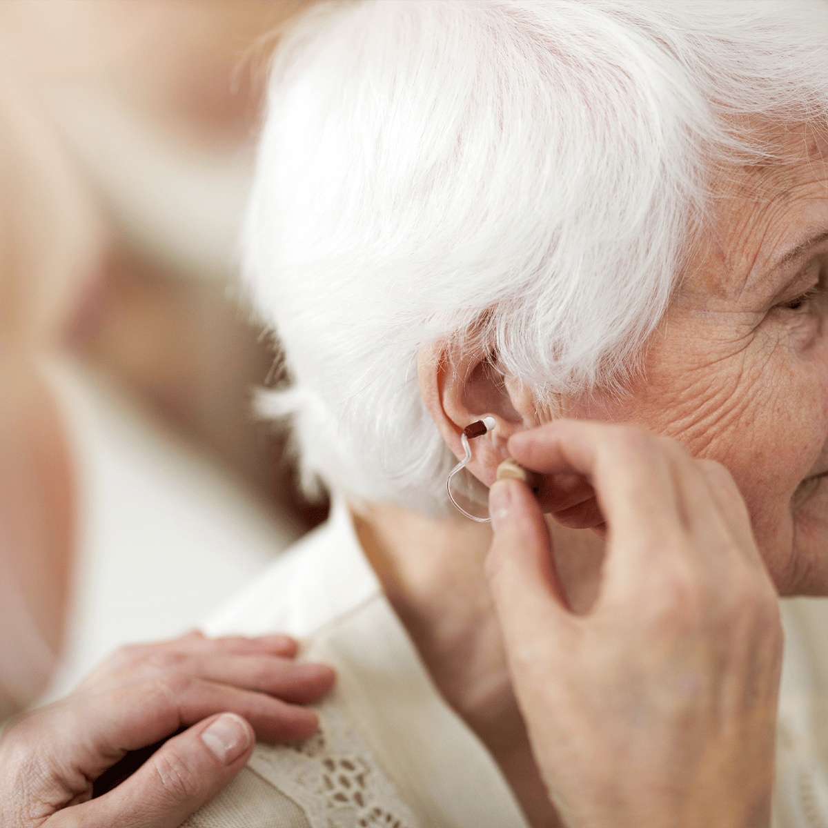 Caregiver inserting a hearing aid into a senior woman's ear