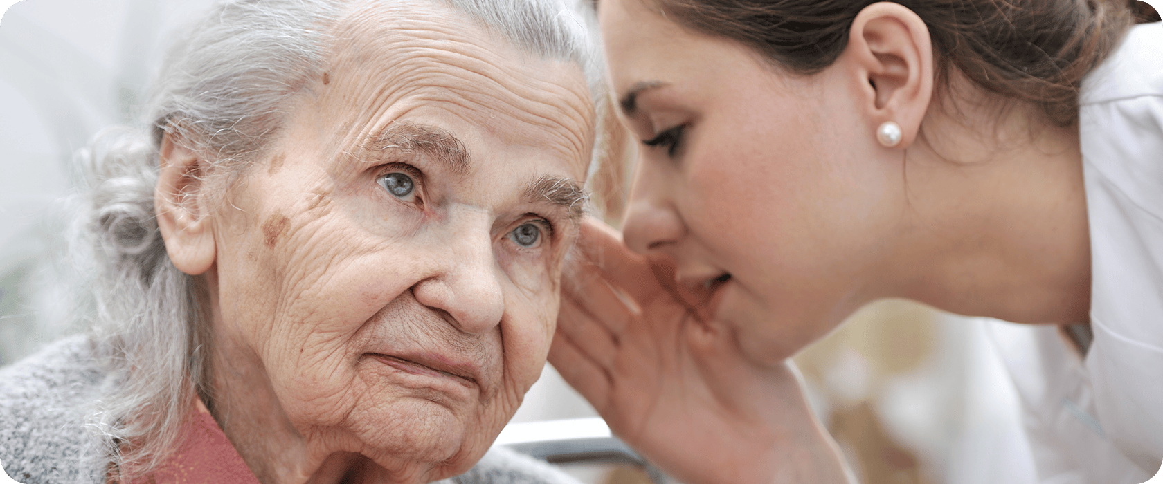 An elderly woman with gray hair listens intently as a younger person whispers into her ear, creating an intimate and caring moment.