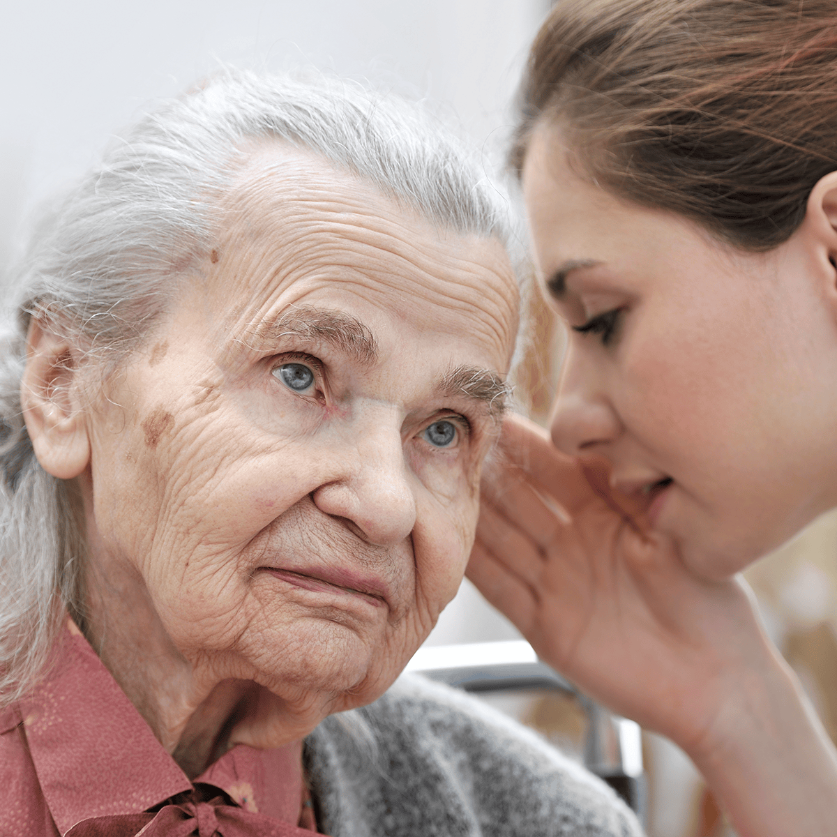 An elderly woman listens intently while a younger woman whispers to her, creating a scene of intimate communication and connection.