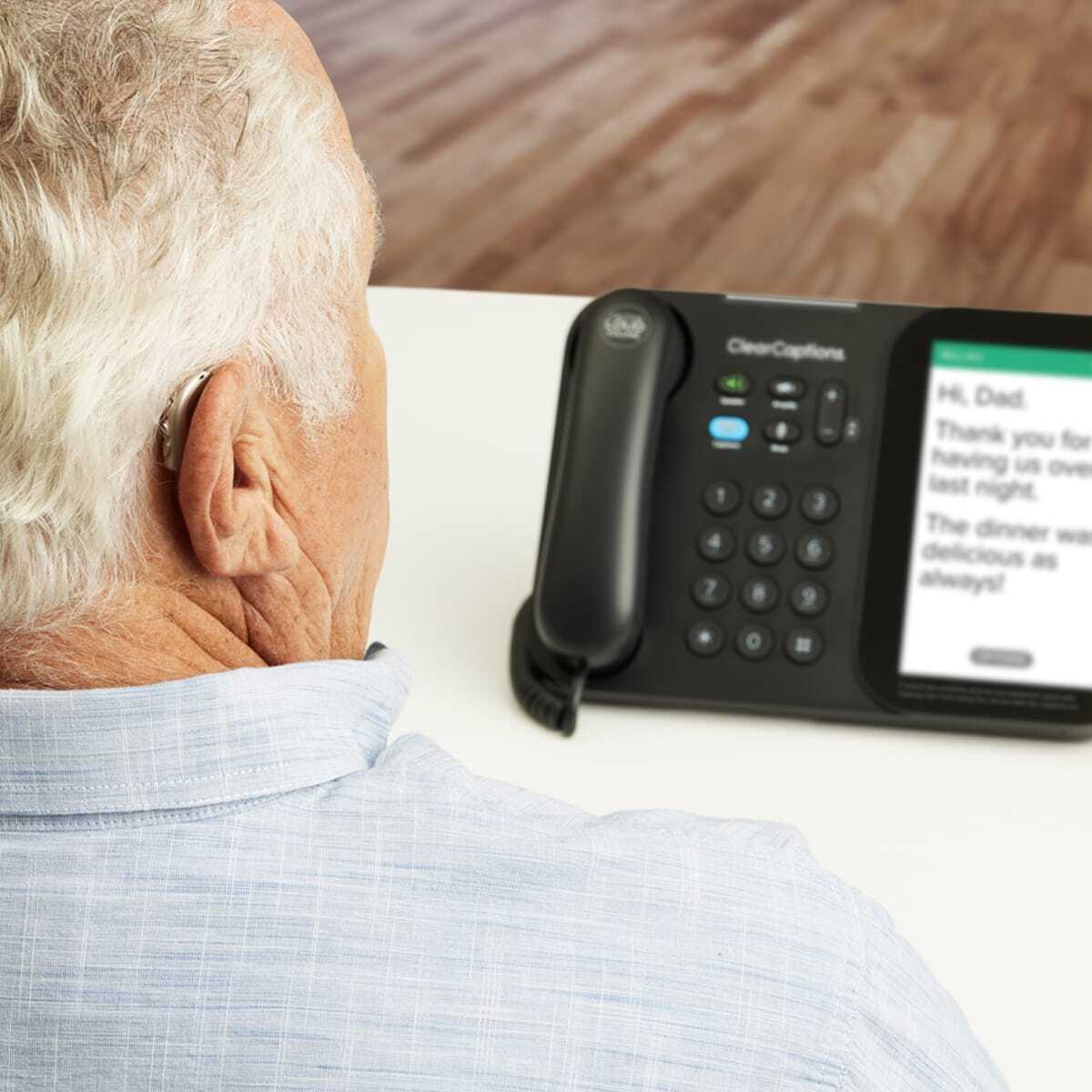 Senior with hearing aid using the ClearCaptions caption phone