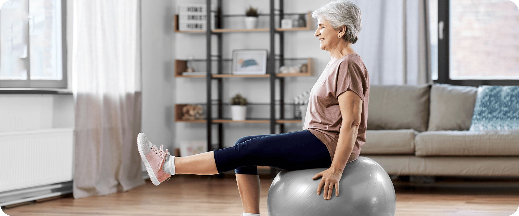 A person balances on an exercise ball, extending one leg forward in a living room. A shelf displaying plants and decor is in the background. Text: "Home Sweet Home."