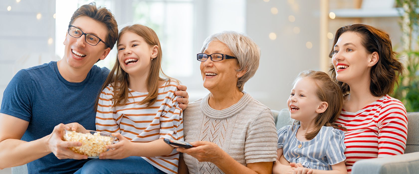Senior woman sitting on a couch, holding a remote control and eating popcorn
