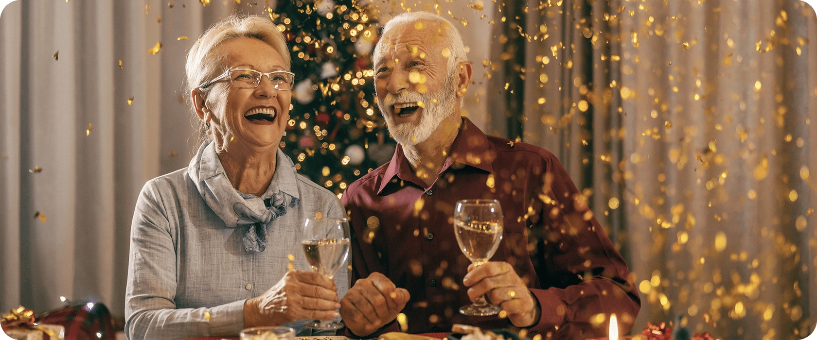 Senior couple laughing as golden confetti falls during a Christmas dinner party