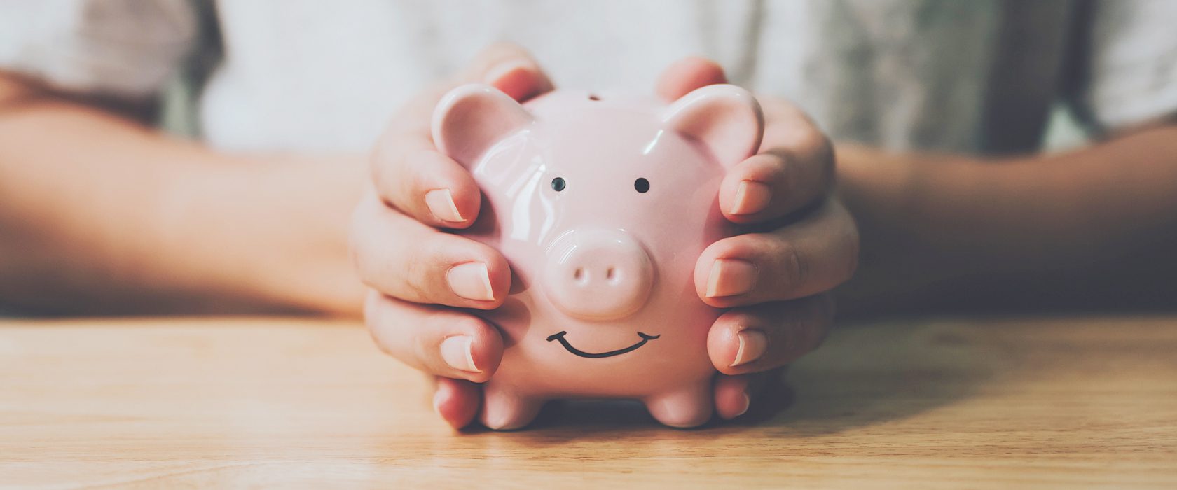 J2501_TRS_1680x700 Hands holding a piggy bank
