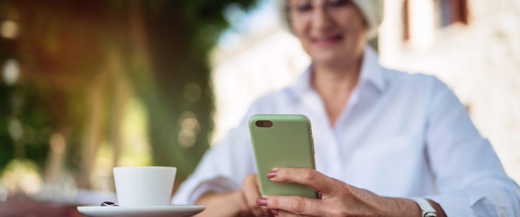 J2653_Mobile-Captions-1680×700-1 Senior woman smiling while using a cell phone