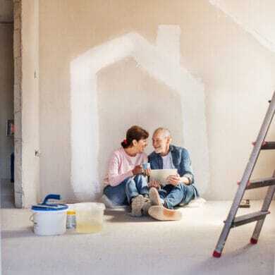 Senior couple sitting on the floor of a home under renovation, smiling at each other
