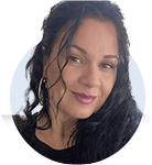 A person with long, dark hair and hoop earrings, facing the camera, smiling slightly, appears against a neutral background in a portrait-style photograph.