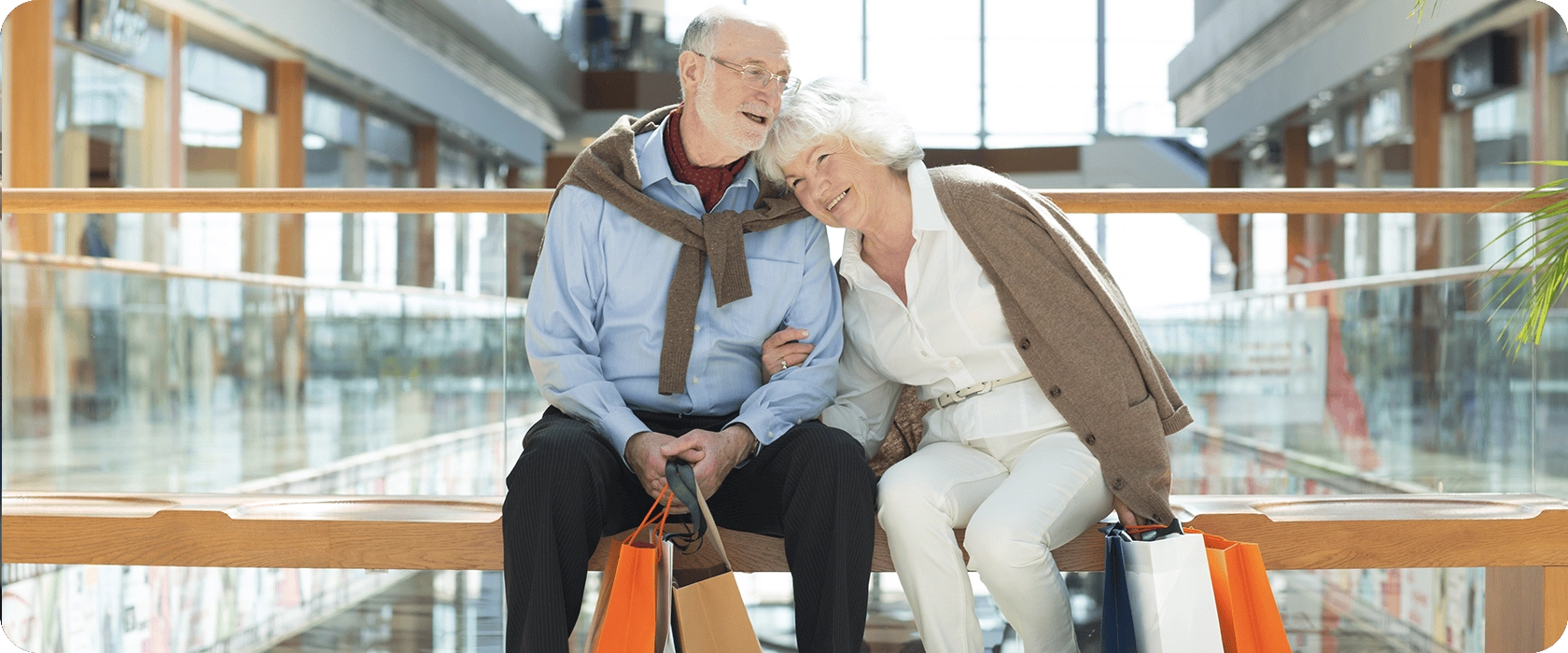Two people sit on a bench, facing a serene lake with boats and mountains in the background, enjoying the peaceful scenery.