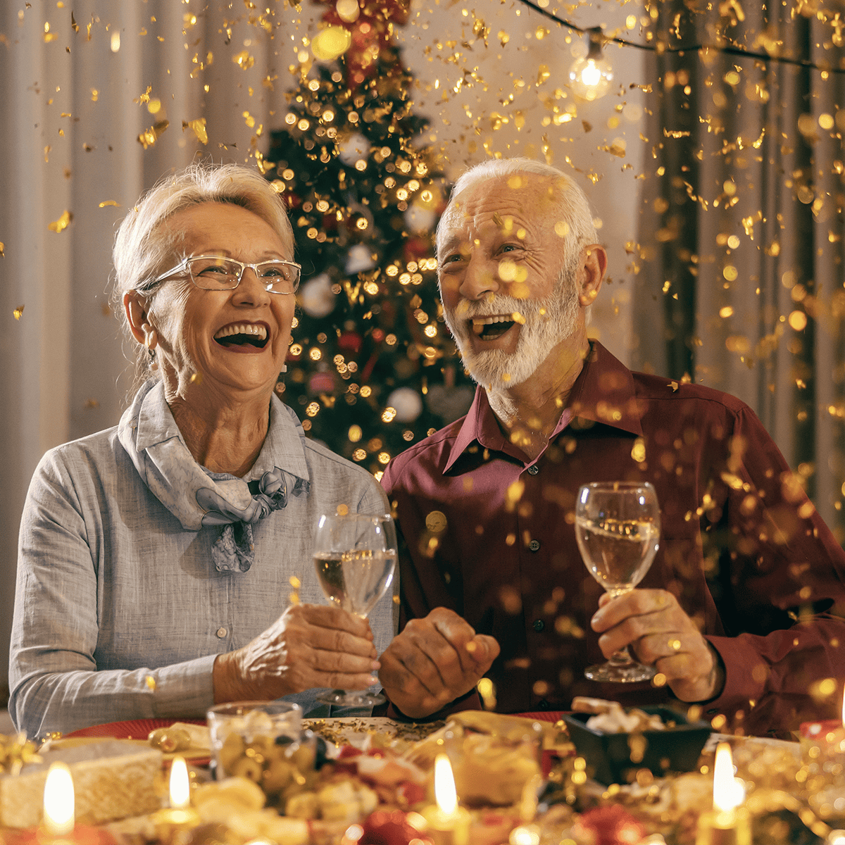 Senior couple laughing as golden confetti falls during a Christmas dinner party