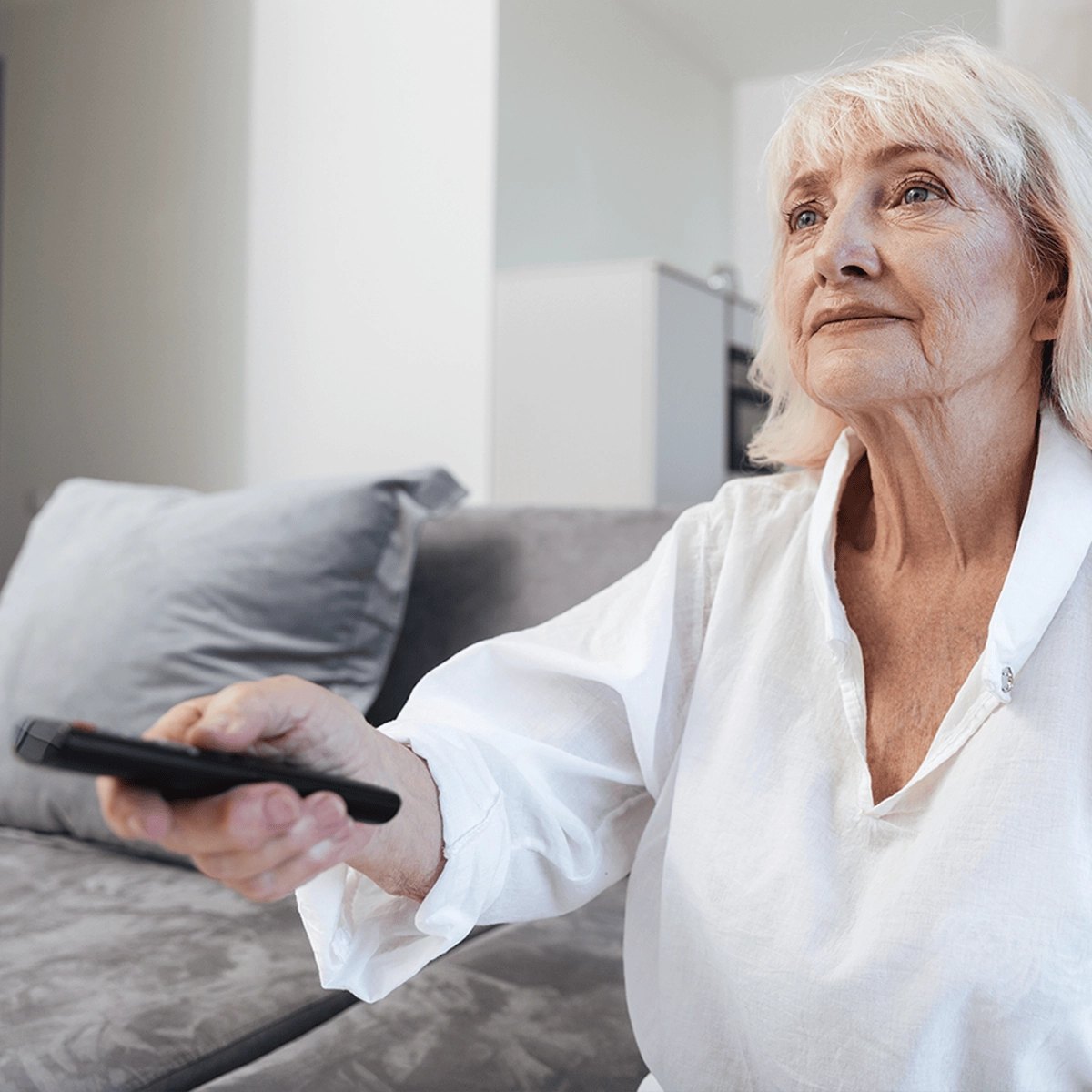 Senior woman sitting on a couch, holding a remote control, watching television