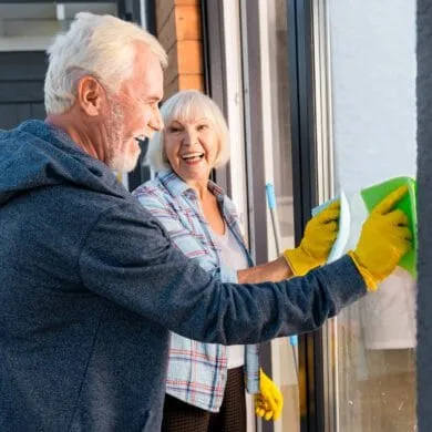 Senior couple smiling at each other while cleaning a window