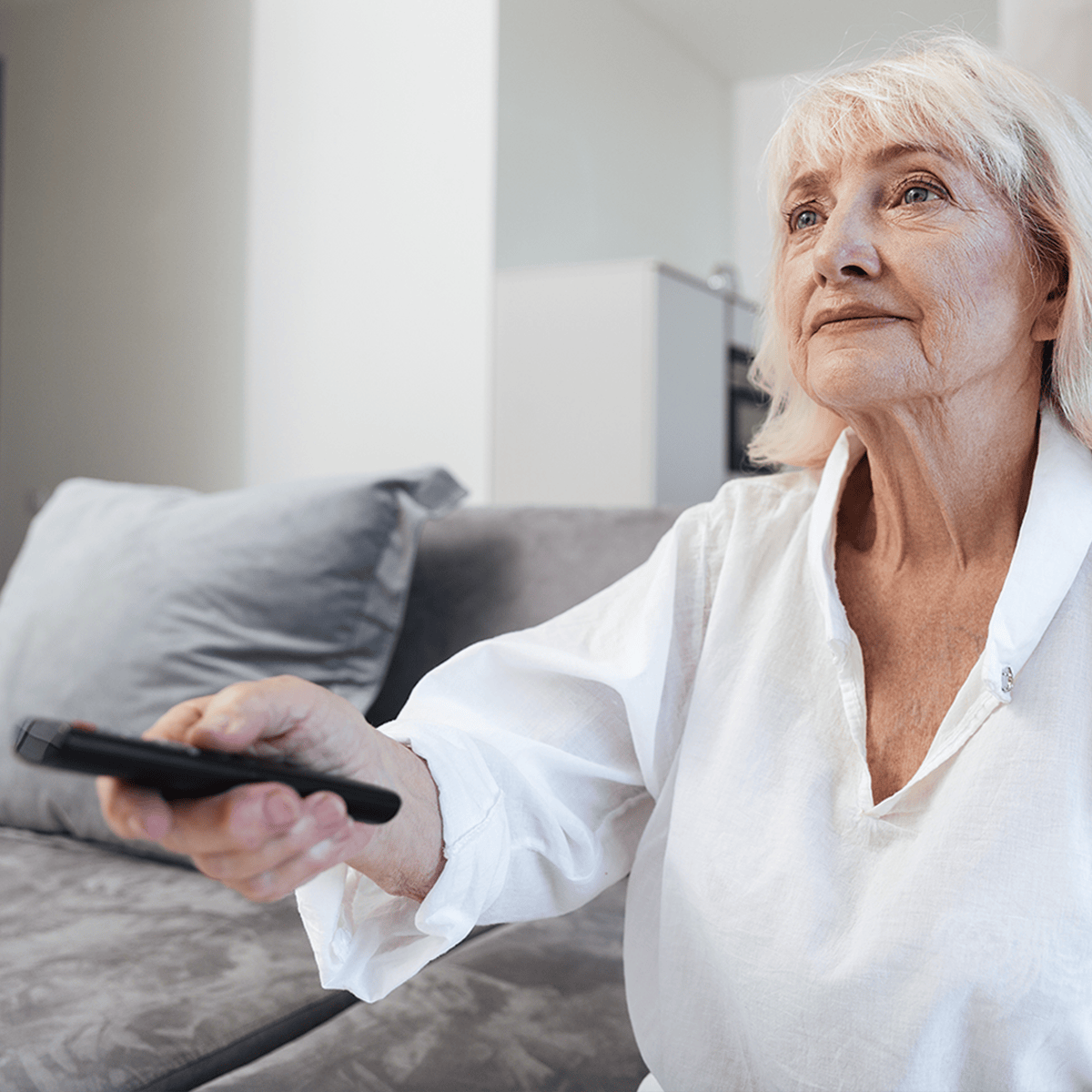 Senior woman sitting on a couch, holding a remote control, watching television