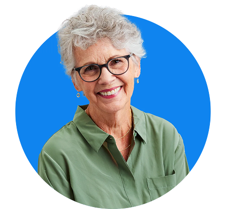 J3623_Header 1 An elderly person, with a soft smile, holds a hand to their ear as if listening attentively, seated indoors with blurred furniture and floral decor in the background.